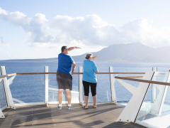 A couple is looking at the cost which is able to see from a platform at the front of the ship.